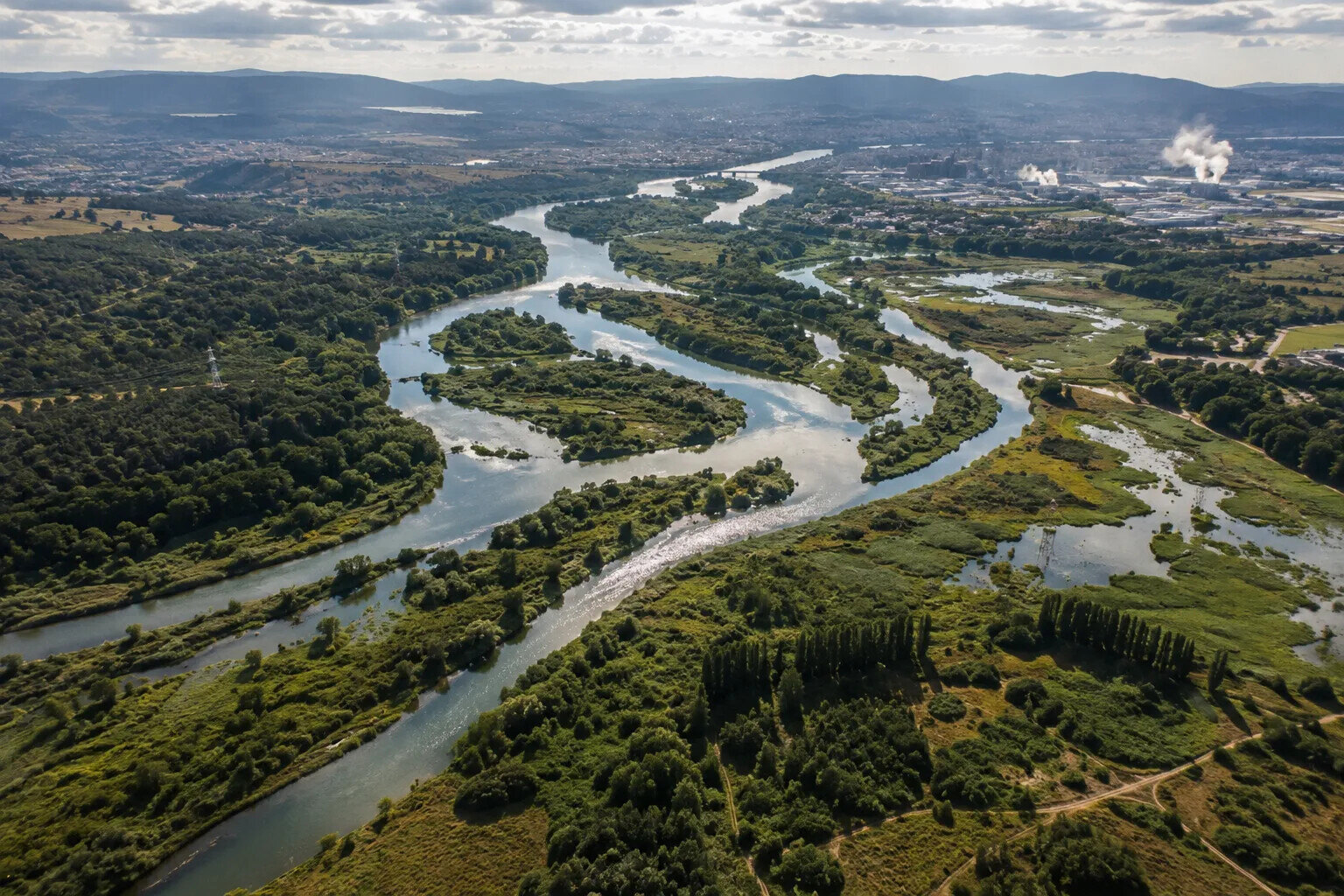 Aerial view of a river system flowing through forests, wetlands and developed landscapes, illustrating ecological interconnection and humanity's relationship with the natural world.